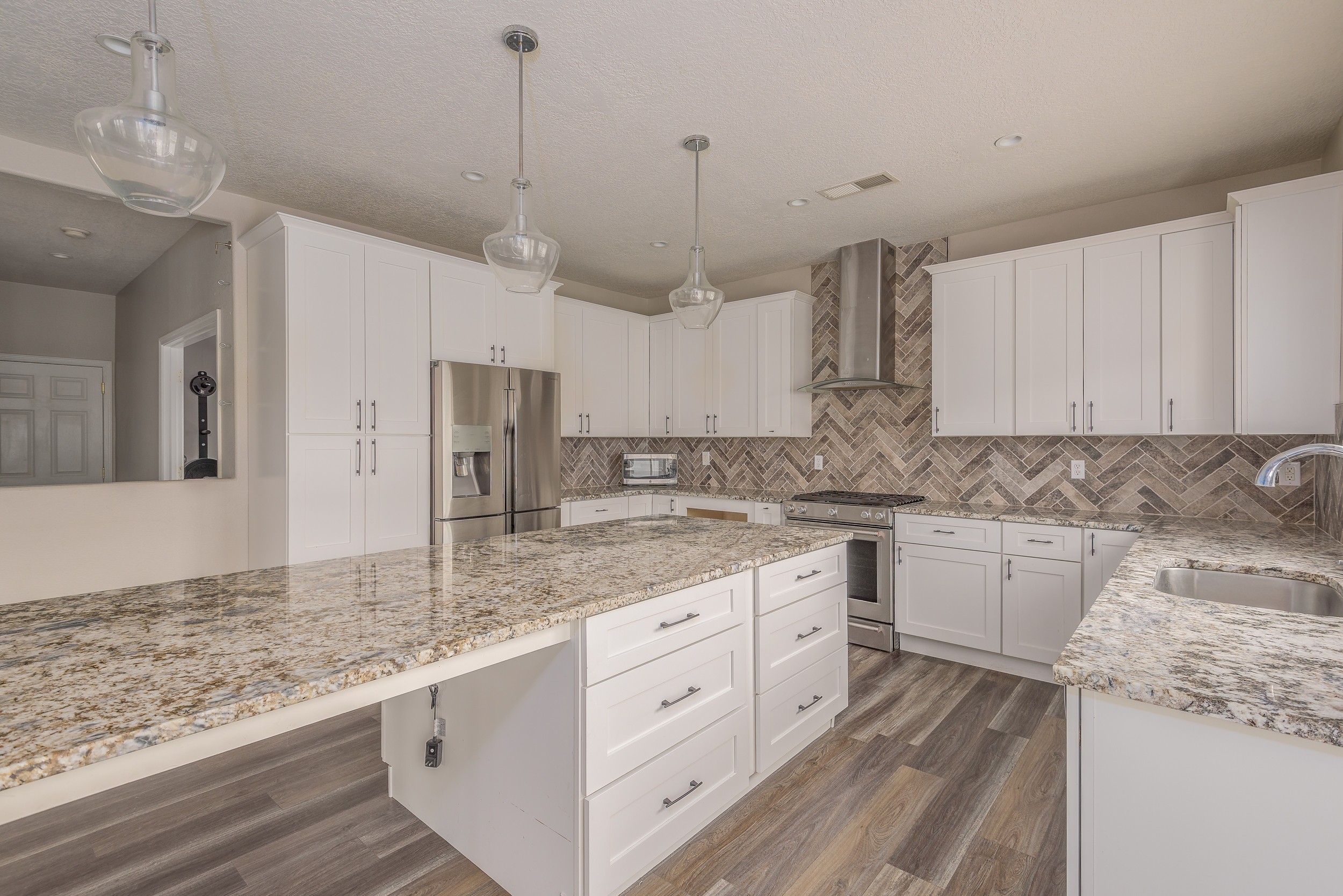 White shaker kitchen with granite counters, glass globe pendants and herringbone backsplash