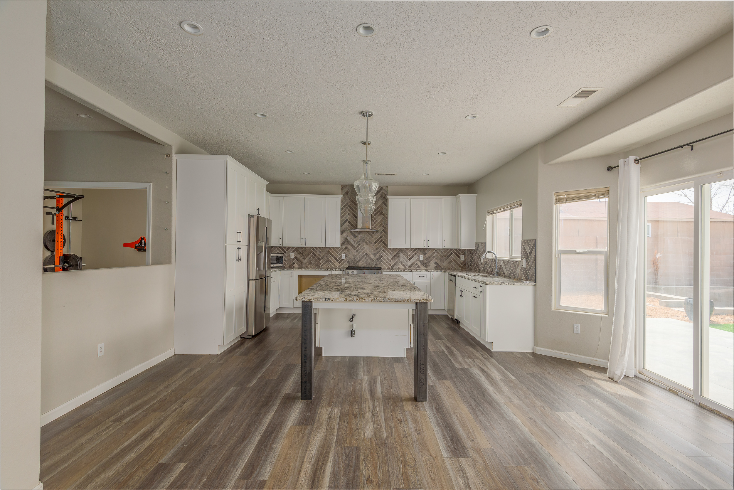Open white kitchen with granite island, herringbone tile backsplash and wood-look flooring